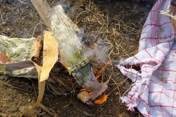 Kleine Flamme und Rauch aus Zunder und Rinde auf dem Boden