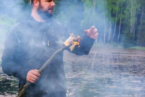 Kleines Bodenfeuer auf einem Stock, Rauch zieht über Wasserfläche
