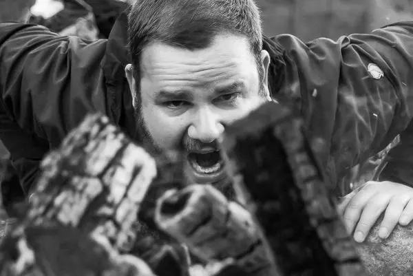 Mann beugt sich über glühende Holzscheite und ruft laut