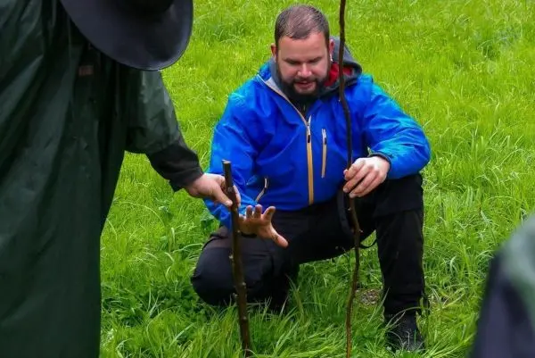 Mann kniet im Gras und hält einen Stock, während er auf einen anderen zeigt