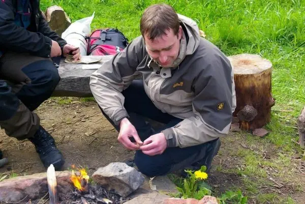 Mann kniet neben einem kleinen Feuer und bereitet Zunder vor