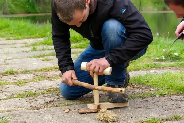 Mann nutzt eine Feuerbohrmaschine, um Zunder zu entzünden
