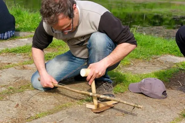 Mann nutzt einen Stock, um mit einem Feuerbohrer Zunder zu entzünden
