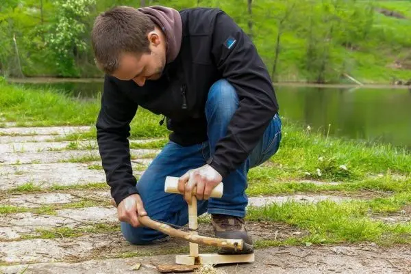 Mann nutzt Holzstück als Hebel, um einen Stock zu bearbeiten