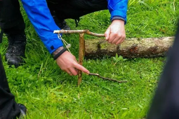 Person baut eine Falle aus Ästen auf dem Gras
