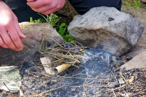 Person bereitet Feuerstelle mit Zweigen vor