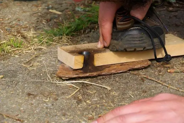 Person drückt mit dem Fuß auf ein Holzstück beim Feuer machen