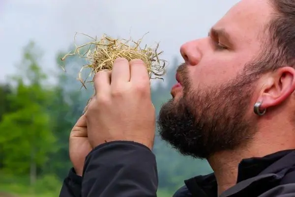Person hält trockenes Gras in der Hand und bläst darauf