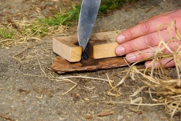 Person schneidet Holzstücke mit einem Messer auf dem Boden