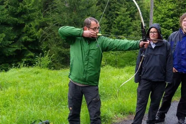 Person zielt mit einem Bogen auf ein Ziel, während andere zuschauen