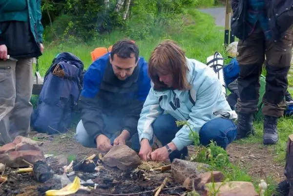 Personen entzünden Feuerstelle mit Zunder und Holzstücken beim Survival Training