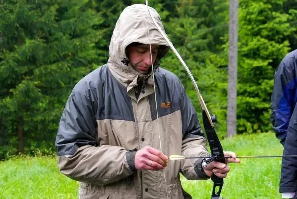 Pfeil wird an einem Bogen gespannt, während eine Person in wetterfester Kleidung steht
