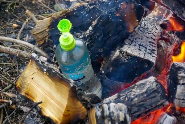 Wasserflasche steht zwischen brennenden Holzscheiten