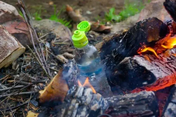Wasserflasche steht zwischen brennenden Holzstücken