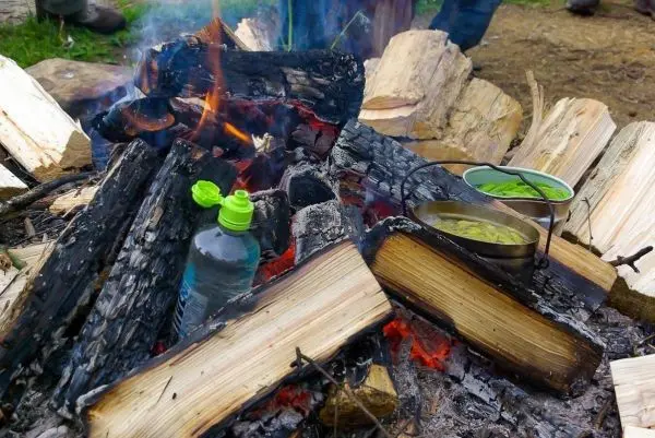 Wasserflasche und Kochtopf stehen neben einem Lagerfeuer
