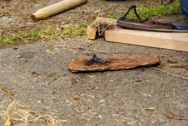 Zunder glimmt auf einem Holzstück neben Werkzeugen und Unterlagen