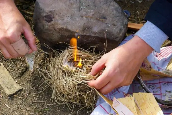 Zunder glimmt in einem Zundernest, während Hände es bearbeiten
