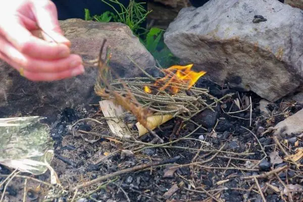 Zunder glimmt zwischen Steinen, Hand hält brennenden Zweig