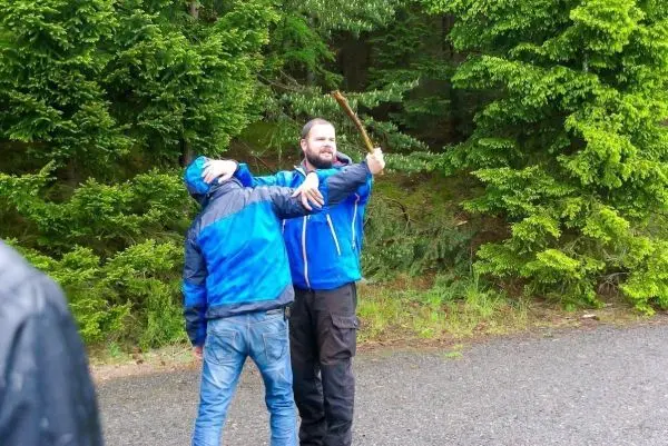 Zwei Personen in blauen Jacken, eine hält einen Stock und umarmt die andere