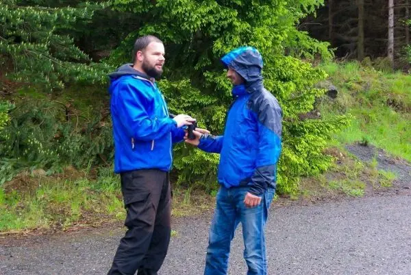 Zwei Personen in blauer Regenjacke tauschen ein Gerät aus