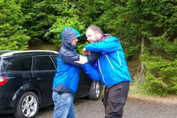 Zwei Personen üben eine Technik zur Selbstverteidigung neben einem Auto