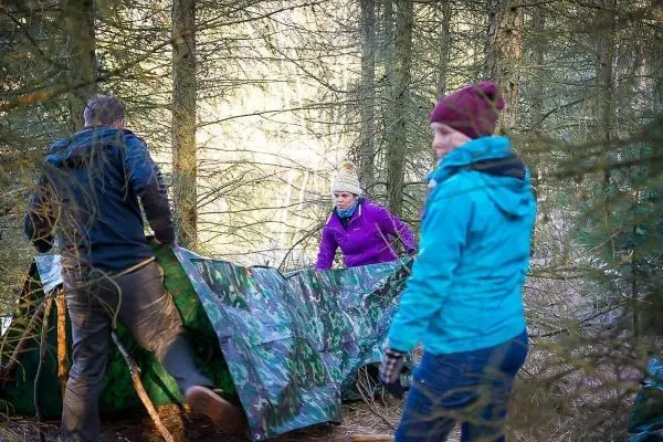 Drei Personen bauen eine Tarp-Notunterkunft im Wald auf