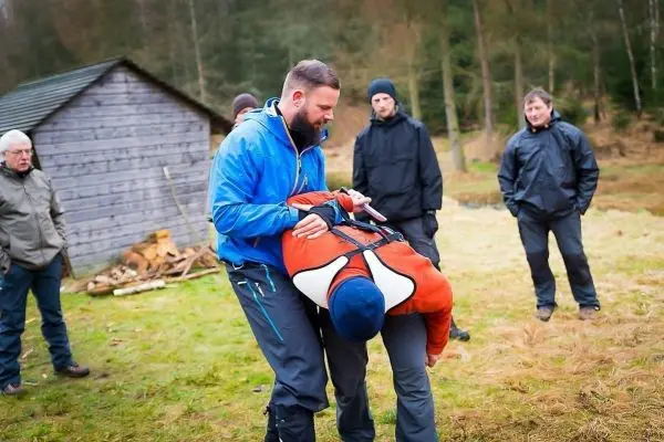 Ein Mann demonstriert eine Tragehilfe mit einem anderen Mann in orangefarbener Jacke