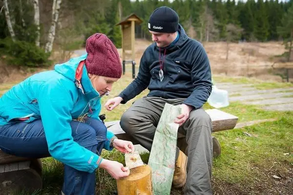 Frau bearbeitet Holzstück, Mann hält Karte und beobachtet