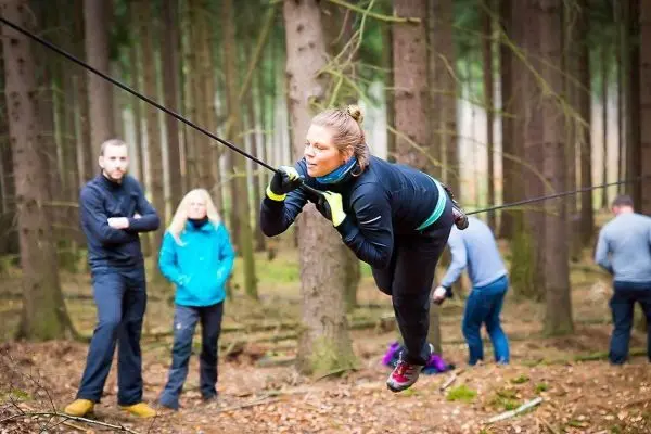 Frau überquert selbstgebaute Seilbrücke zwischen Bäumen im Wald