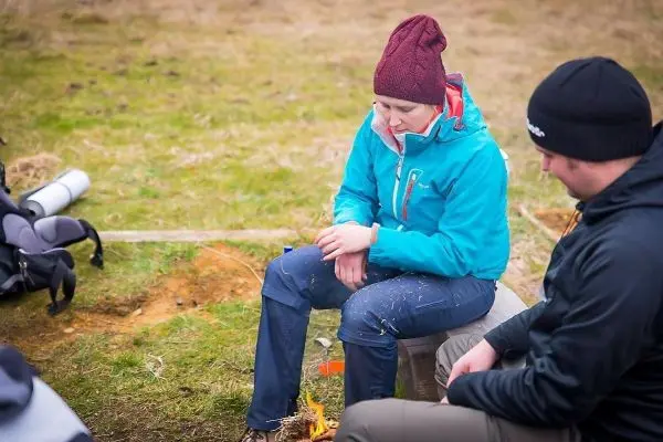Frau zündet Zunder mit Feuerstahl neben kleinem Bodenfeuer