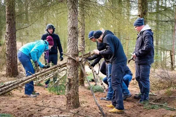 Gruppe baut eine selbstgebaute Konstruktion aus Ästen zwischen zwei Bäumen