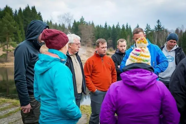 Gruppe diskutiert am Ufer eines Gewässers, umgeben von Bäumen