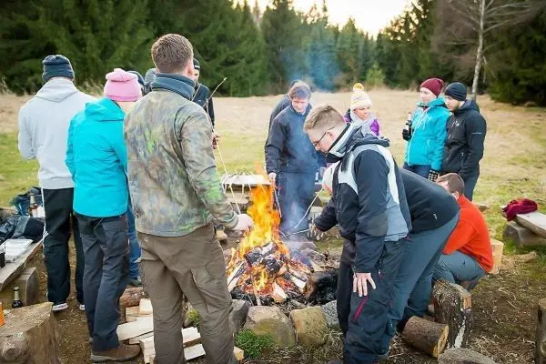 Gruppe um ein Lagerfeuer, einige halten Stock mit Essen über die Flammen