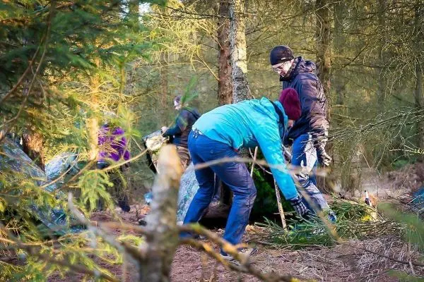 Gruppierung von Personen baut Tarp-Notunterkunft im Wald auf