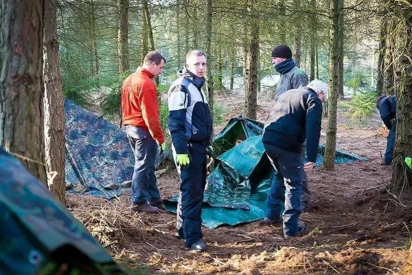 Gruppierung von Personen beim Aufbau einer Tarp-Notunterkunft im Wald