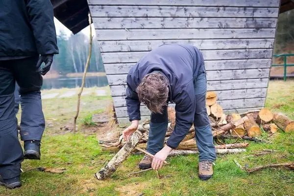 Holzstück wird auf dem Boden untersucht, Holzstapel im Hintergrund