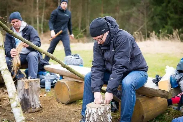 Mann bearbeitet Holzstück mit einem Messer auf einem Baumstamm