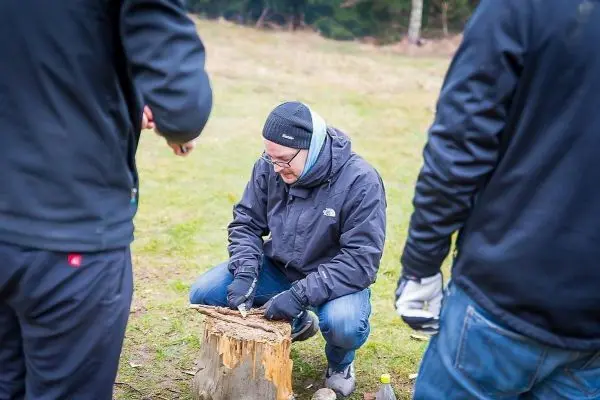 Mann bearbeitet Holzstück mit Messer auf einem Baumstumpf