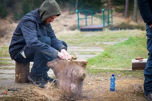 Mann bearbeitet Zunder auf einem Baumstumpf mit einem Messer