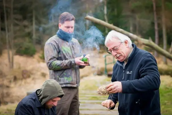 Mann bereitet Zundernest vor, während andere beobachten und Rauch aufsteigt