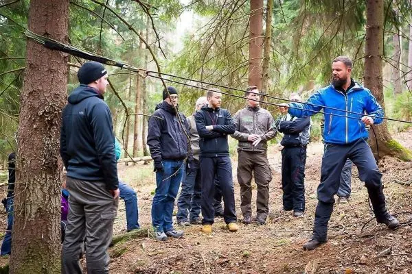 Mann demonstriert Seilquerungstechnik zwischen Bäumen, Gruppe beobachtet aufmerksam