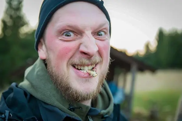 Mann mit Bart und Mütze zeigt ein breites Grinsen und hält etwas zwischen den Zähnen