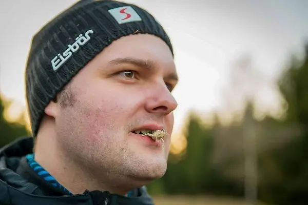 Mann mit Gras im Mund steht vor unscharfem Hintergrund