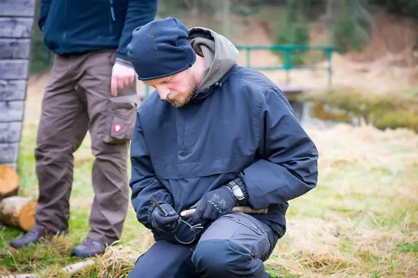 Mann schnitzt mit einem Messer an einem Holzstück im Freien