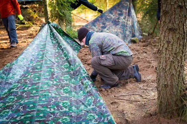 Mann überprüft die Befestigung einer Tarp-Notunterkunft im Wald