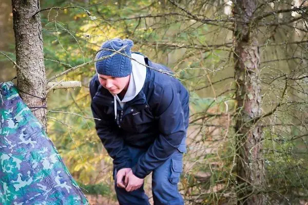 Mann überprüft eine Tarp-Notunterkunft zwischen zwei Bäumen