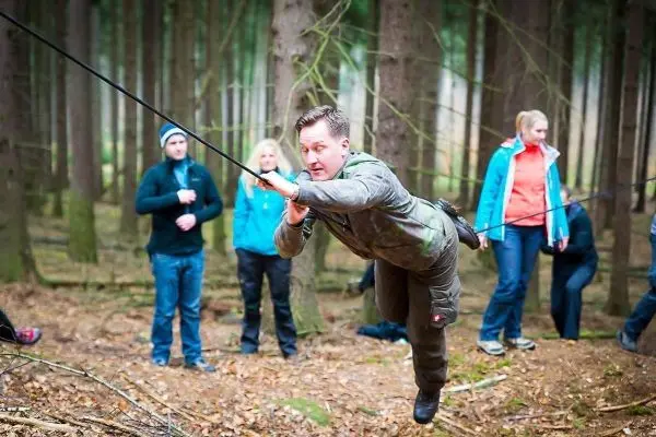 Mann überquert selbstgebaute Seilbrücke zwischen Bäumen im Wald