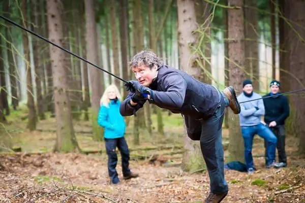 Mann überquert selbstgebaute Seilbrücke zwischen Bäumen im Wald