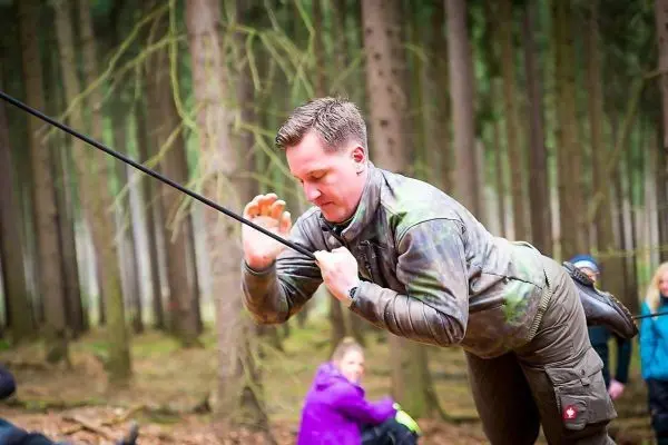Mann überquert selbstgebaute Seilbrücke zwischen Bäumen im Wald