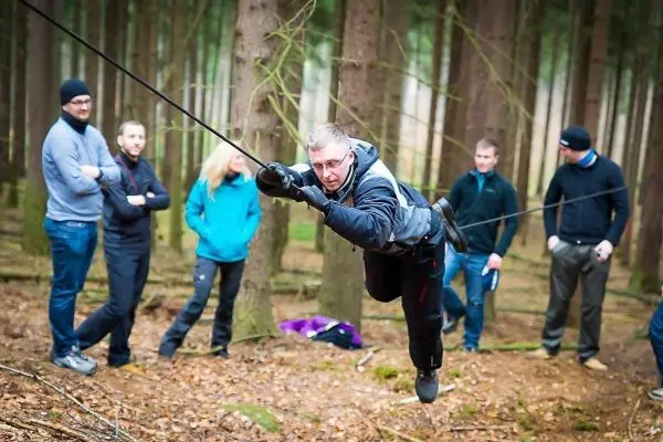 Mann überquert selbstgebaute Seilbrücke zwischen Bäumen, Zuschauer beobachten